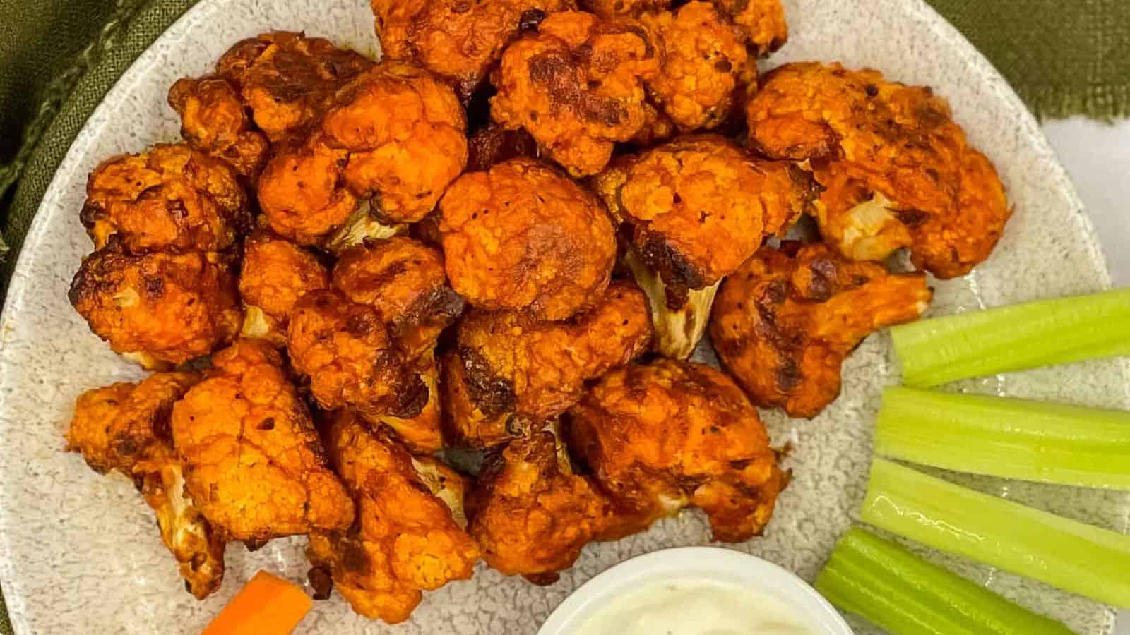 A plate of cauliflower wings with dipping sauce and celery.