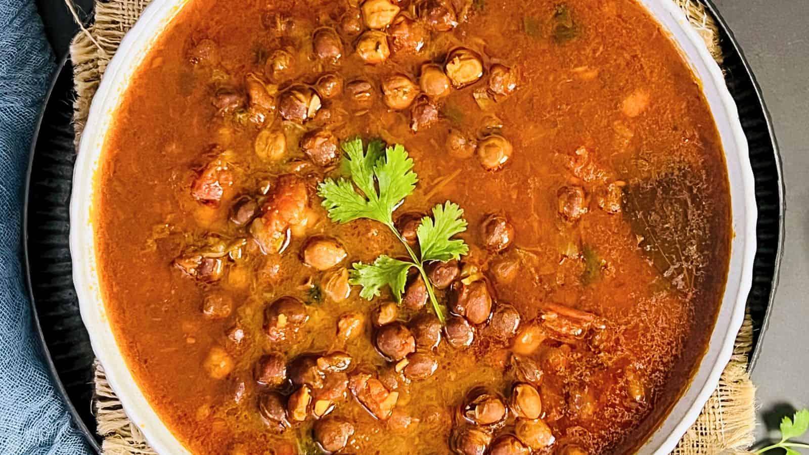 A bowl of Kala Chana Curry garnished with fresh cilantro, served on a dark textured surface.
