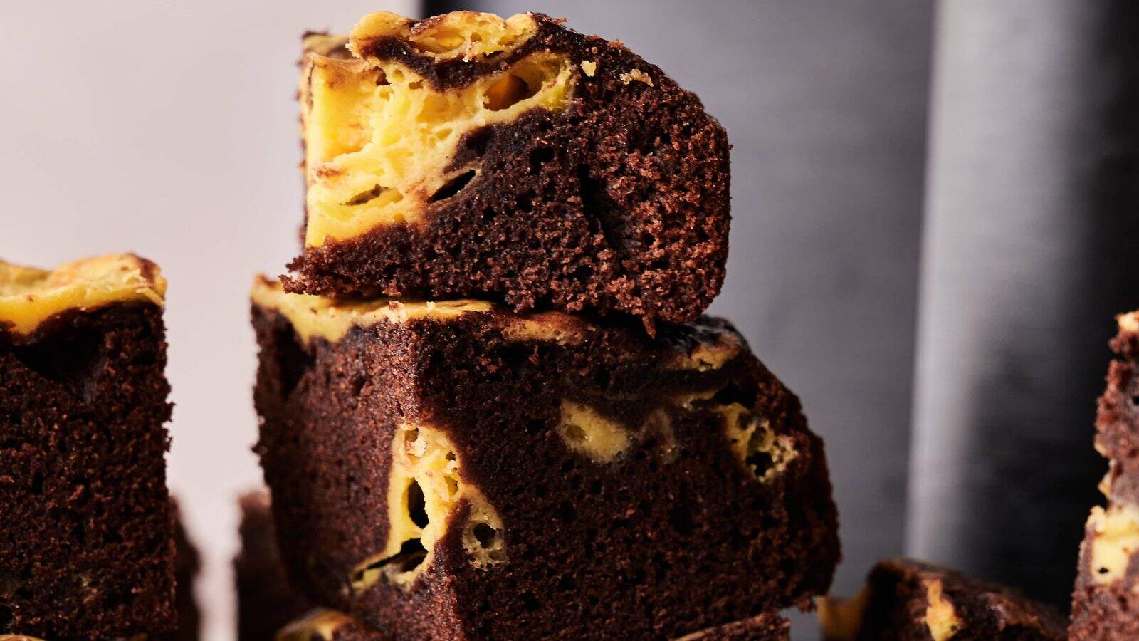 Close-up of stacked chocolate brownies with a yellow cheesecake swirl, showing a moist texture and marbled appearance.