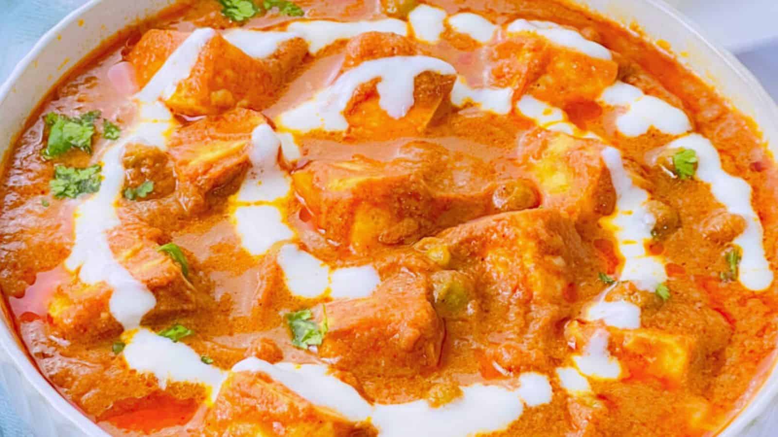 A bowl of Matar Paneer masala garnished with cream and cilantro.