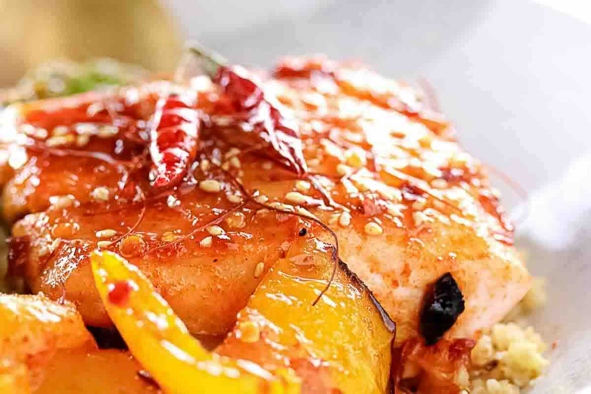Close-up of a cooked salmon fillet topped with sesame seeds, dried red chilies, and sliced yellow bell peppers.