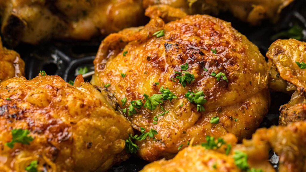 Close-up of crispy, golden-brown roasted chicken thighs garnished with chopped parsley.