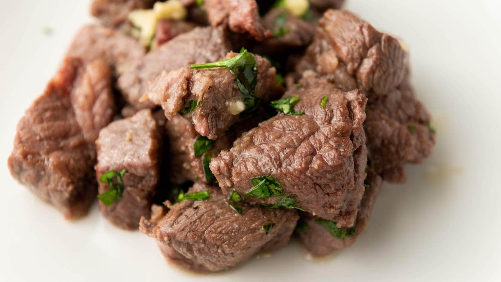 Cooked beef cubes garnished with chopped herbs, served on a white plate.