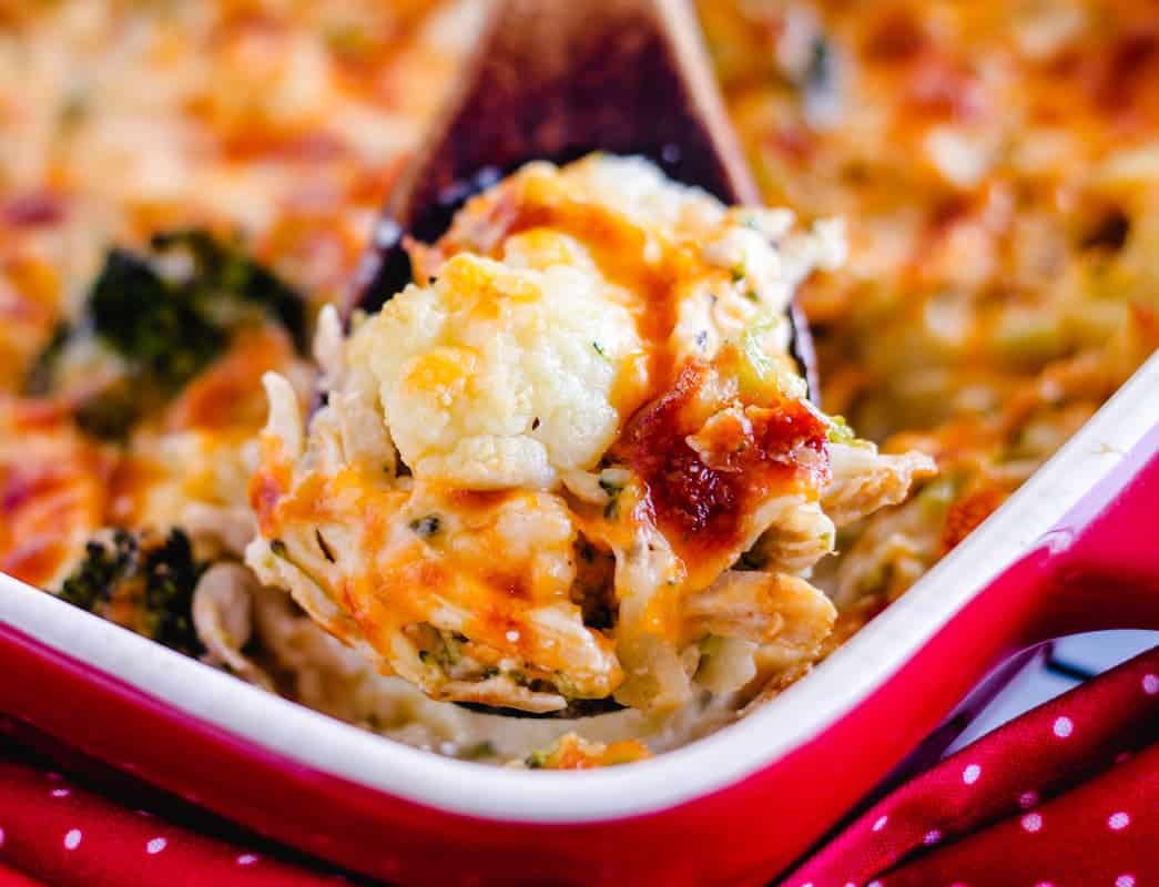A wooden spoon scooping out a portion of cauliflower chicken casserole.