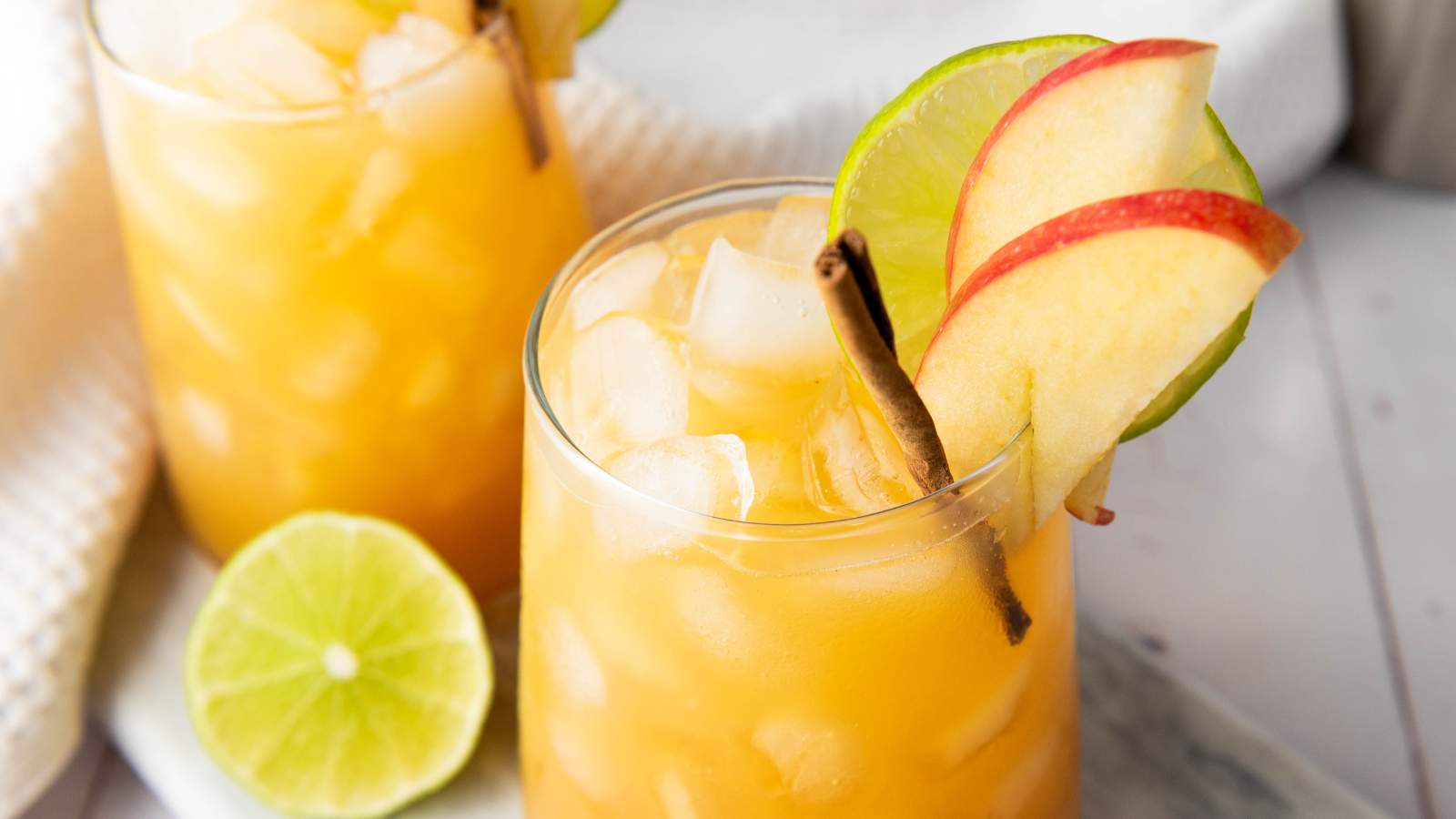 A glass of mocktail iced drink garnished with apple and lime slices and a cinnamon stick.