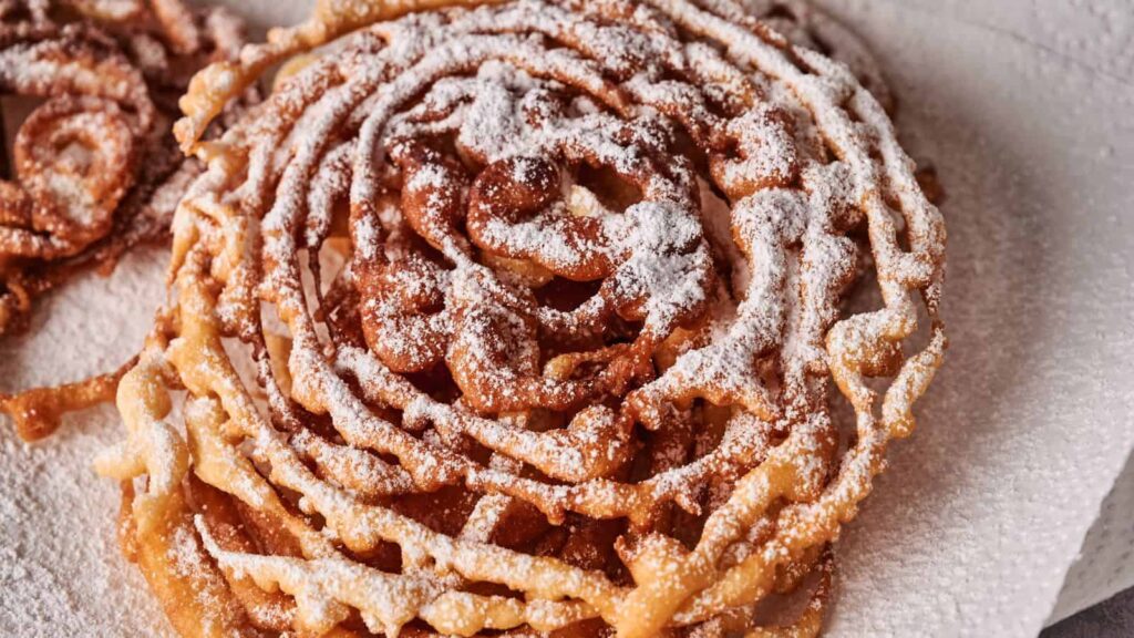 A close-up of a funnel cake topped with powdered sugar, resting on a white paper towel.
