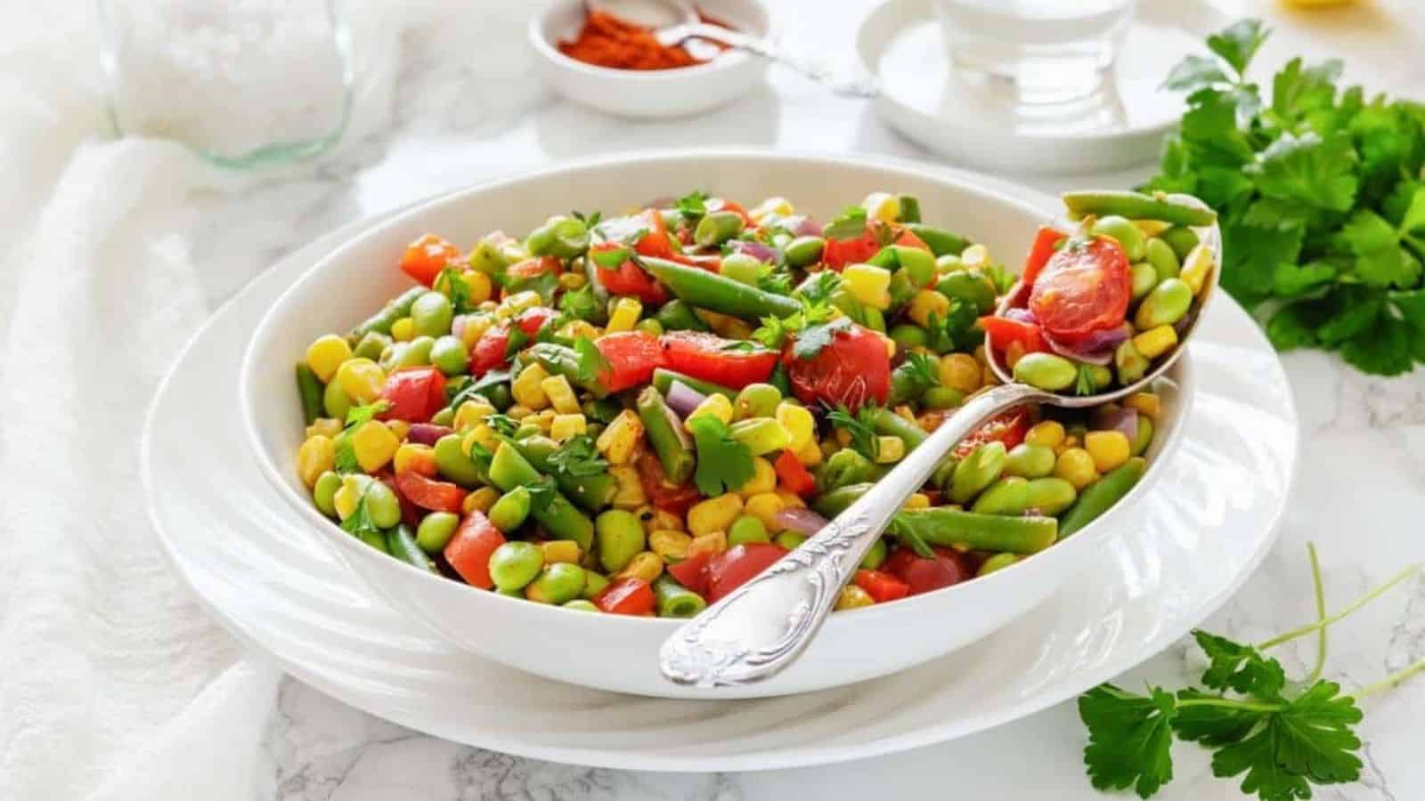 A white bowl filled with Southern Succotash with a serving spoon resting on the side.