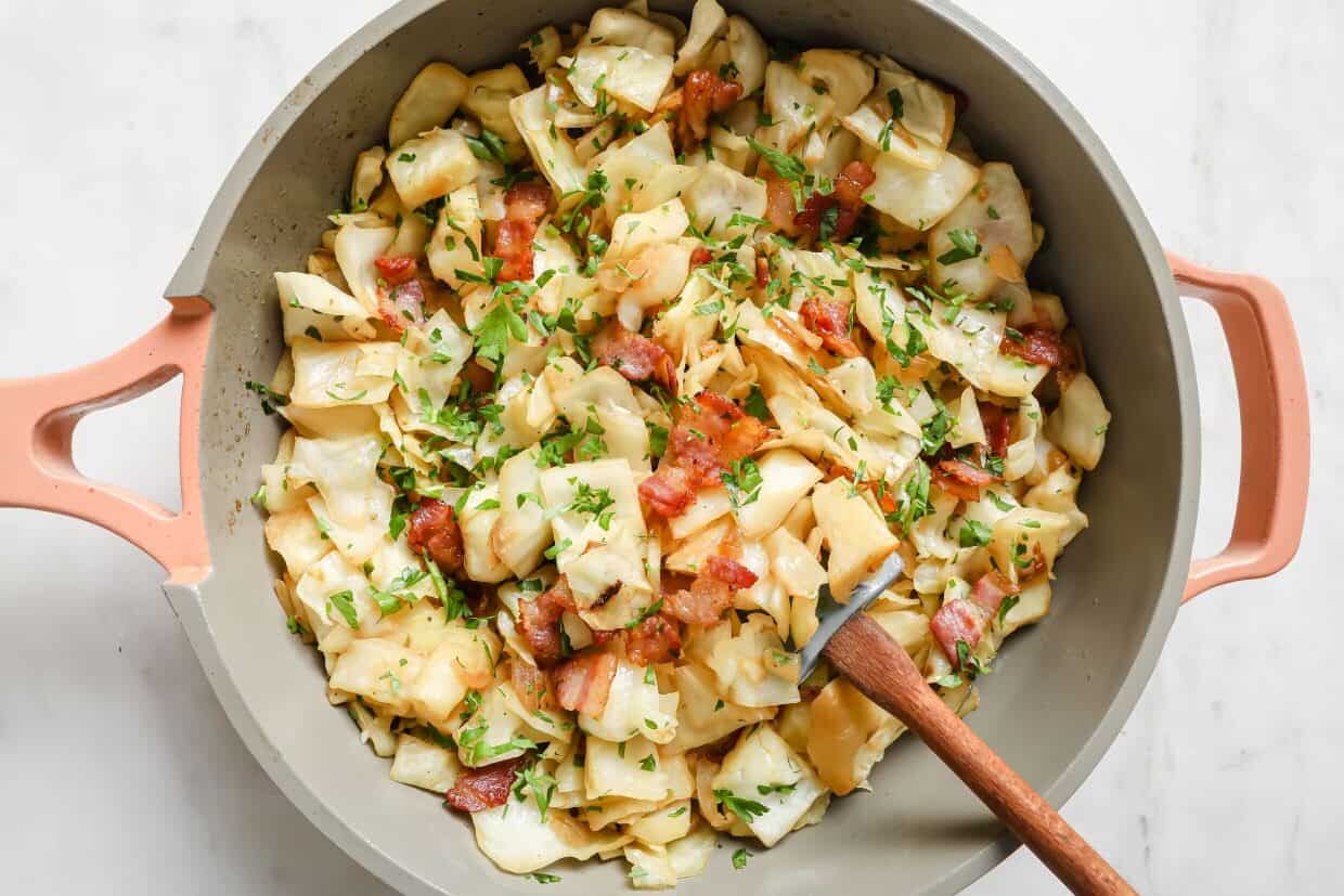 A pan full of bacon and cabbage with a wooden spoon.