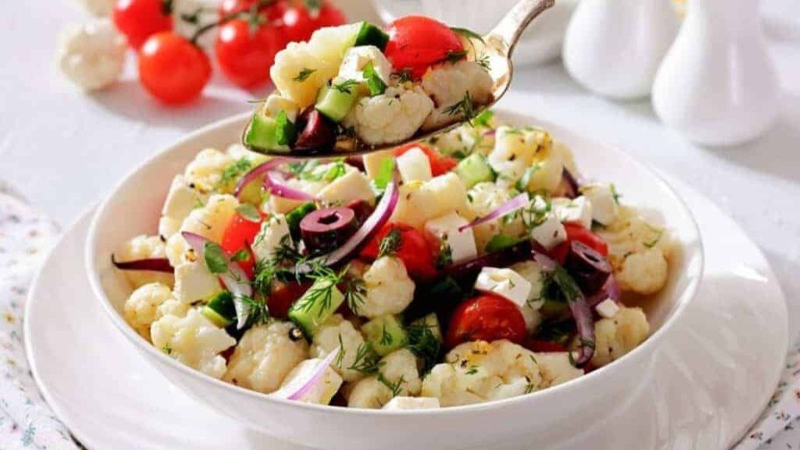 A spoon holds a serving of Greek Cauliflower Salad above the bowl.