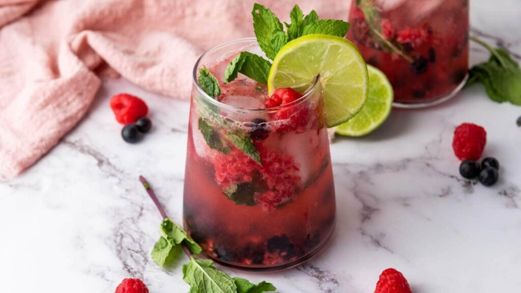 Two glasses of berry mocktail arranged on a marble surface with fresh mint and lime.