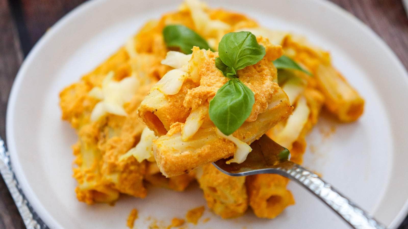 A plate of pumpkin pasta with creamy sauce and melted cheese, garnished with fresh basil.