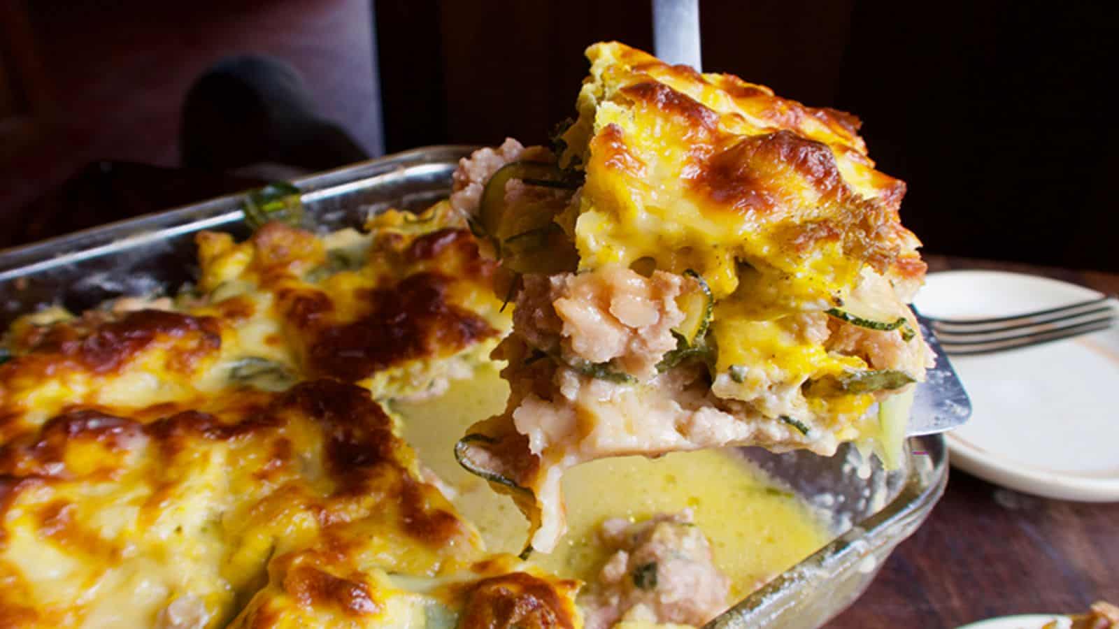 A slice of breakfast lasagna being lifted from a baking dish.