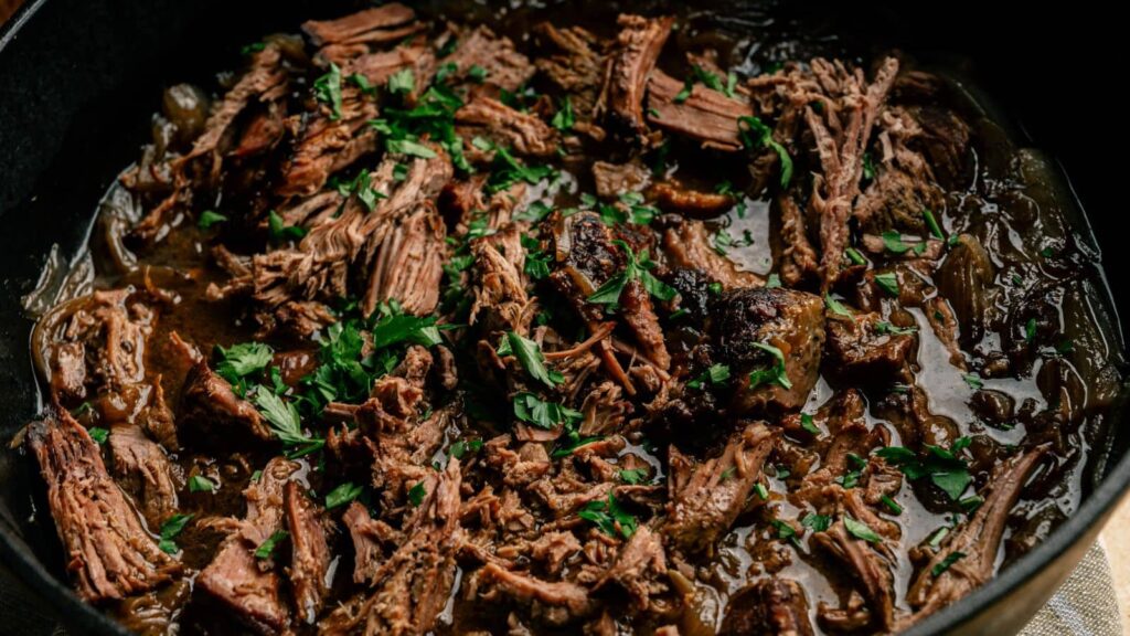 Shredded braised beef with herbs and onions in a dark sauce, served in a black pan.