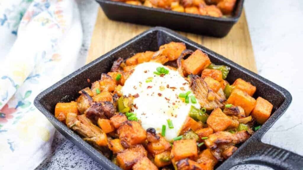 Cast iron skillet with sweet potato hash with pulled pork and garnished with chopped chives.
