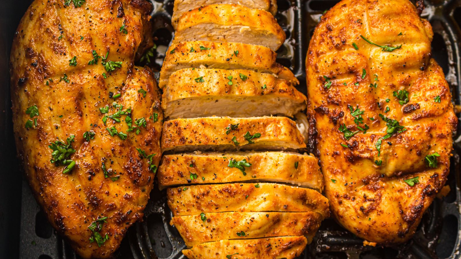 Sliced grilled chicken breast seasoned with herbs and pepper, displayed on an air fryer tray.
