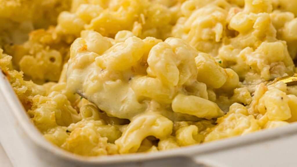 Close-up of creamy baked macaroni and cheese in a white dish, with a serving spoon lifting a portion.
