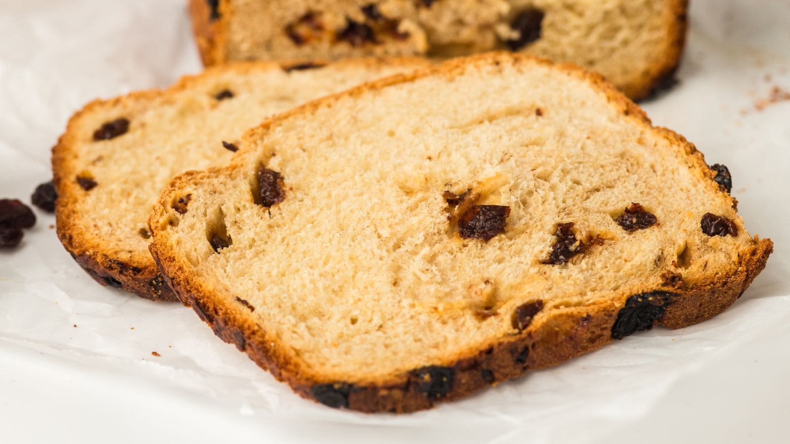 Two slices of raisin bread are placed on a white surface, showing a golden-brown crust and raisins baked into the soft interior.