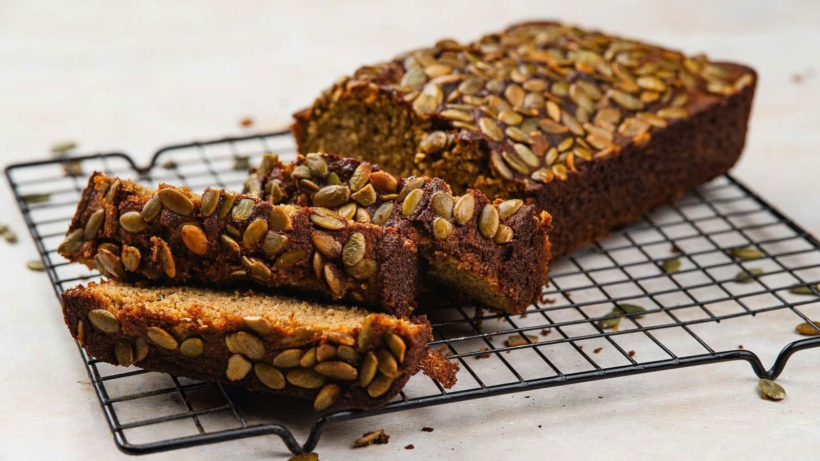 A loaf of pumpkin bread partially sliced on a wooden surface, with visible pumpkin seeds on top and inside the bread slices.