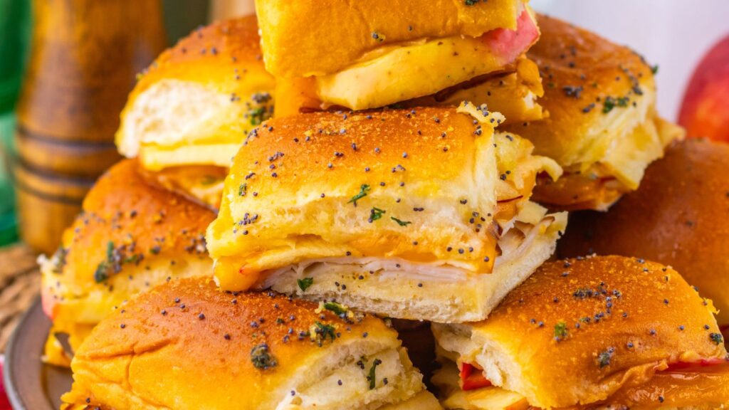 A stack of turkey and cheese slider sandwiches on a plate next to a red apple.